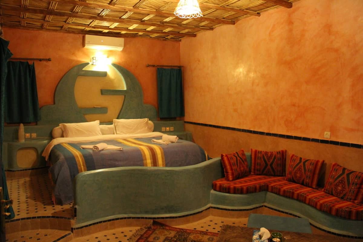 Una habitación con cama, sofá, un gran elemento decorativo en la pared y ventilador de techo.