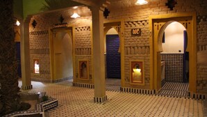 Un vestíbulo de hotel con temática marroquí, que presenta paredes de piedra, arcos y suelo de baldosas.