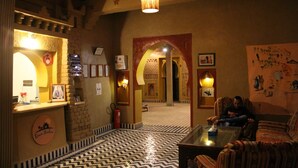 Un hall de hotel con mostrador de recepción, suelo estampado y una zona de estar con mesa de vidrio.