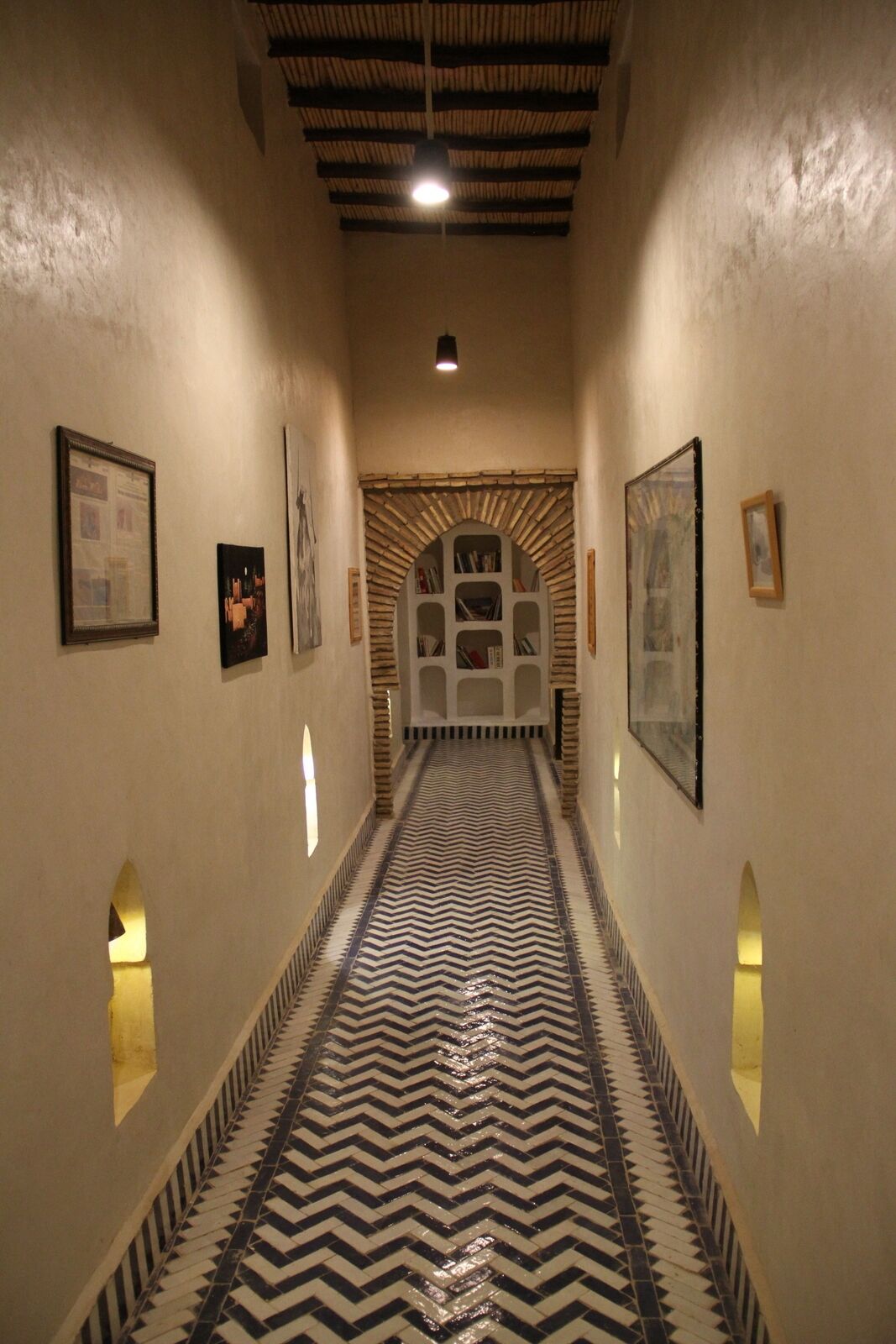 A hallway with patterned flooring, framed artwork on the walls, and a central arched bookshelf.