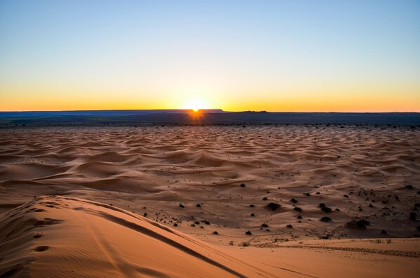 A desert landscape with sand dunes and a sunset.