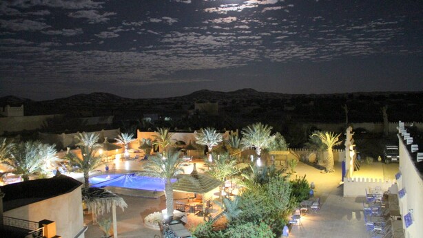 Un resort con piscina, palmeras y montañas al fondo bajo un cielo nocturno.