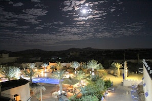 A resort with a pool, palm trees, and a mountainous backdrop under a night sky.