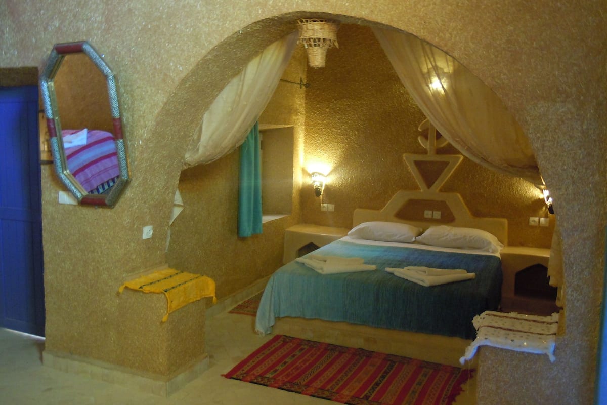 Un dormitorio acogedor, parecido a una cueva, con una cama, un espejo y una pequeña mesa.