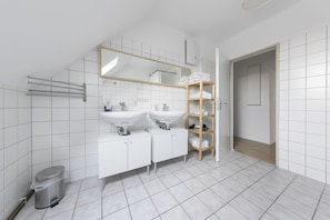 A modern bathroom with two sinks, a mirror, a towel rack, and a wooden shelf.