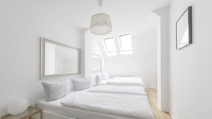 Ein modernes, minimalistisches Schlafzimmer mit zwei Betten, einem großen Spiegel und einem kleinen Holfnachtkästchen.