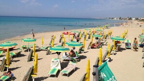 A beach with rows of sun loungers and umbrellas, a clear sky, and the ocean in the background. - Baglio il Giovinetto (Marsala)