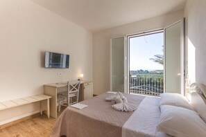A bedroom with a bed, a desk, a chair, a TV, and a balcony with a view. - Baglio il Giovinetto (Marsala)