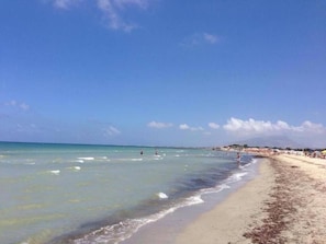 Una playa con agua azul cristalina, orilla arenosa y algunas personas.