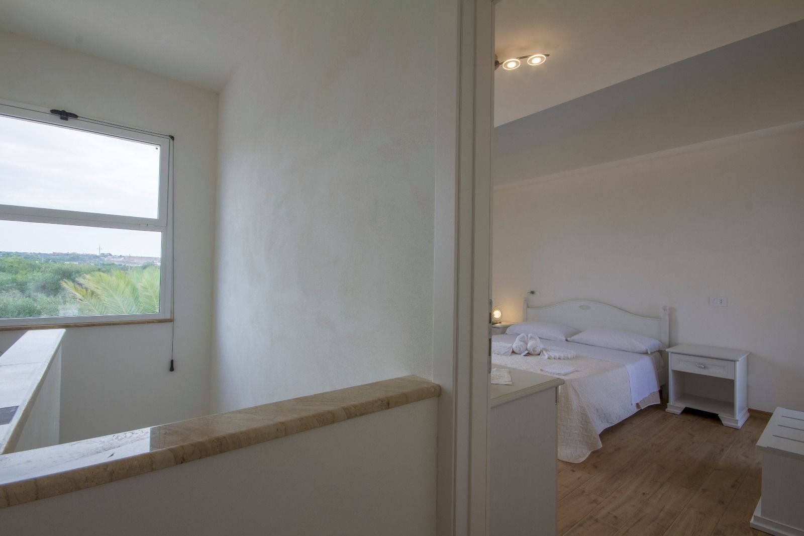 Een slaapkamer met een bed, nachtkastjes en een raam met uitzicht op groen.