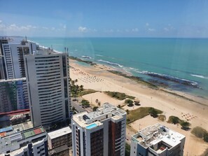 Un edificio de gran altura con piscina en la azotea y una playa al fondo.