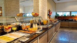 A buffet setup with various food items and beverages, a glass display case, and a brick wall. - Flat Beach Class Executive (Recife)