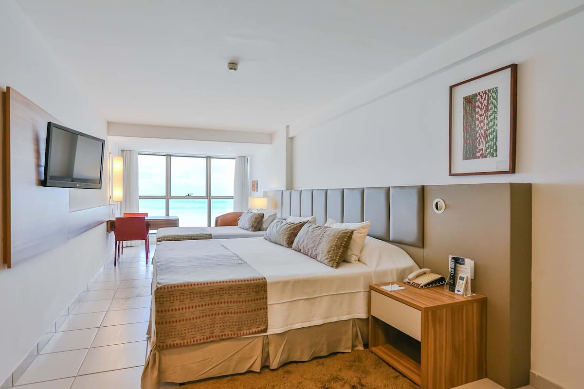 Une chambre d’hôtel moderne dotée d’un grand lit, d’un bureau, d’une chaise, d’une télévision et offrant une vue sur la mer.