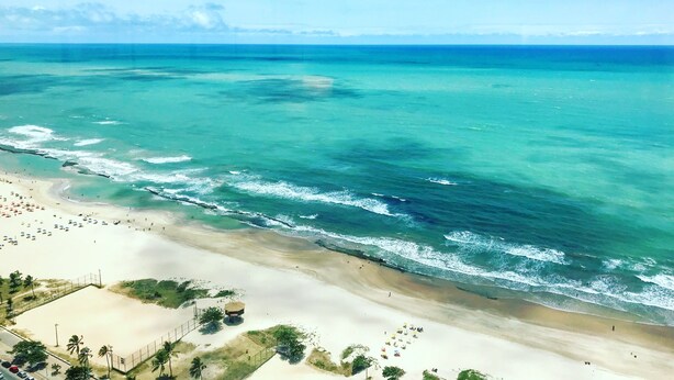 A beach with clear turquoise waters, a sandy shore, and a few umbrellas and people. - Flat Beach Class Executive (Recife)