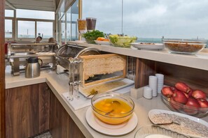 A buffet setup with various food items, a sandwich maker, and a view of the sea. - Marcello Hotel (Istanbul)