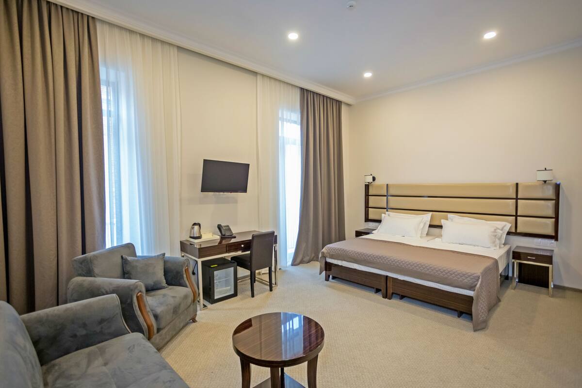 A hotel room with a bed, a desk, a chair, a TV, and a small table.