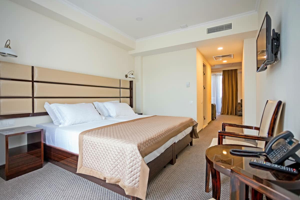 A hotel room with a large bed, bedside tables, a desk with a telephone, and a TV mounted on the wall.