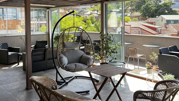 Un espace extérieur aménagé avec des meubles en osier, un fauteuil suspendu et une vue sur le quartier environnant.