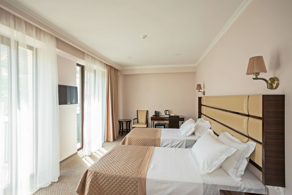 A hotel room with two beds, a desk, a chair, and a television.