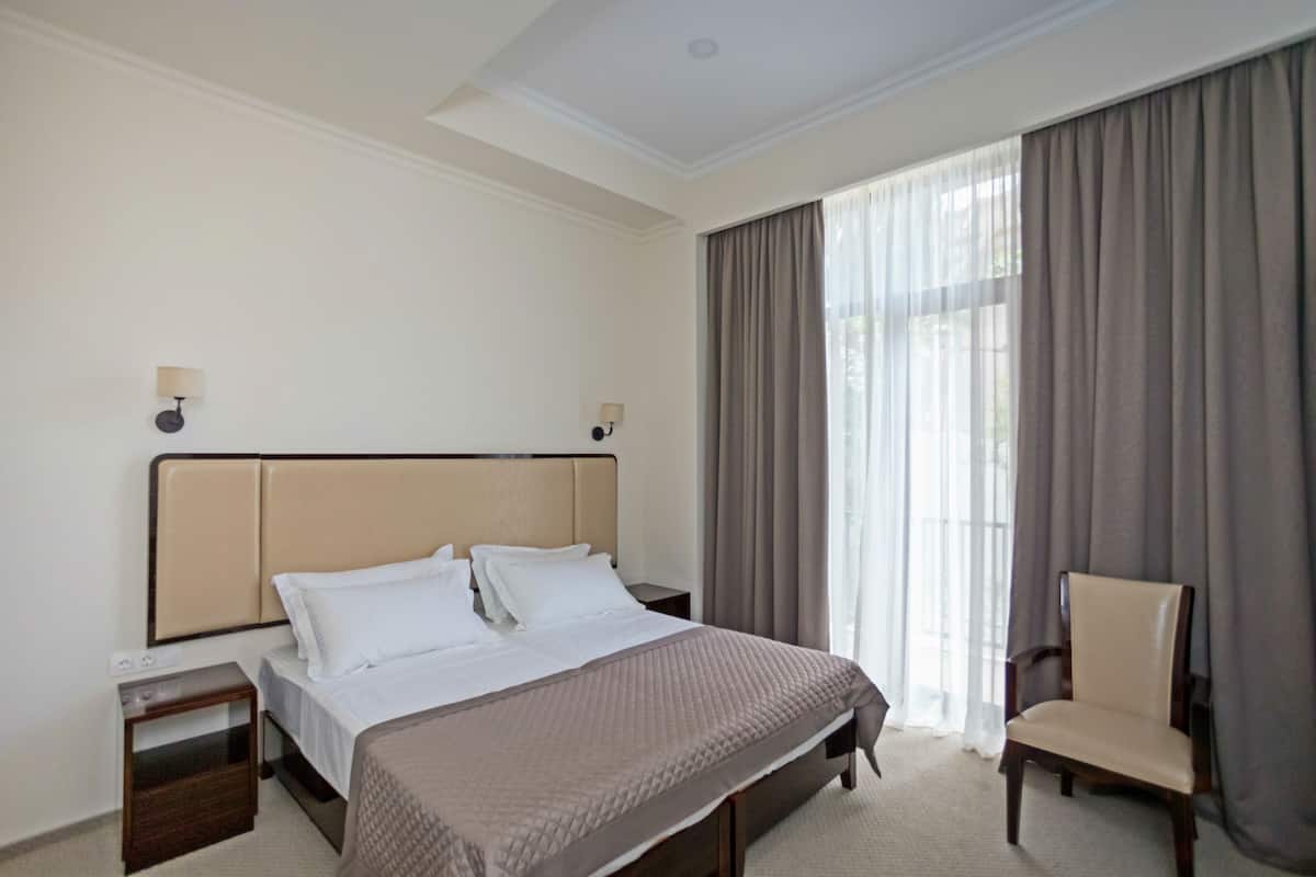 A hotel room with a bed, two bedside tables, a chair, and a large window with curtains.
