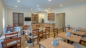 Un espace repas avec des tables et des chaises en bois, un comptoir central doté d’un évier et des étagères en bois intégrées.