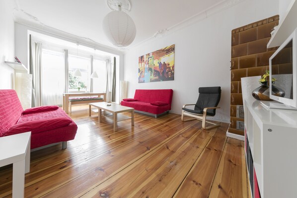 A modern living room with wooden flooring, a red sofa, a black chair, and a white coffee table.