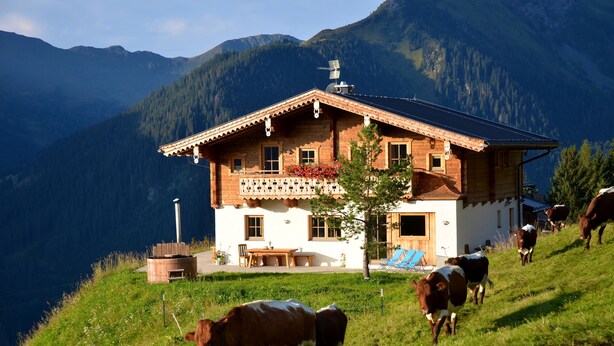 A chalet with a balcony, surrounded by a grassy hillside and mountains.