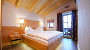 A wooden bed with white bedding, a nightstand, a wall-mounted lamp, and a window with curtains.