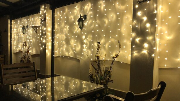 A dining area with a glass table and chairs, decorated with string lights and wall-mounted lamps. - Hotel Diter (Sofia)