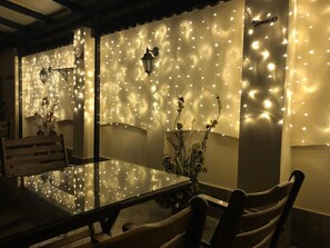A dining area with a glass table and chairs, decorated with string lights and wall-mounted lamps. - Hotel Diter (Sofia)