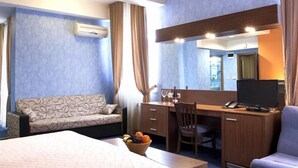 A hotel room with a bed, a desk with a computer, a chair, a sofa, a mirror, and a fruit bowl. - Hotel Diter (Sofia)