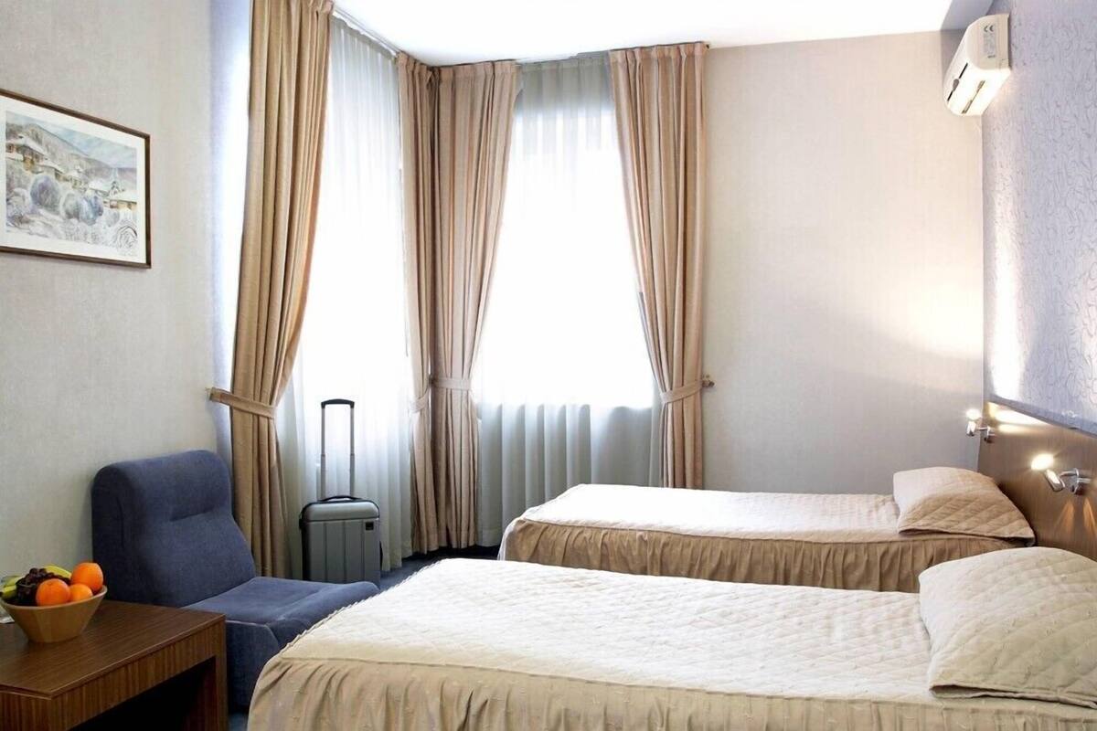 Habitación de hotel con dos camas, una silla, una mesita con frutero y un radiador.