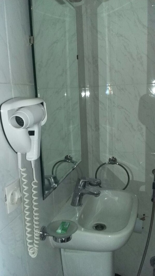 A bathroom with a hairdryer mounted on the wall, a sink with a soap dish, and a mirror. - Hôtel Farouk (Marrakech)