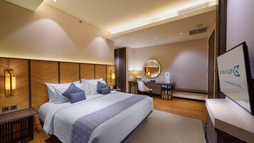 Une chambre d’hôtel moderne avec un grand lit, un bureau, une chaise, un miroir rond et un téléviseur.