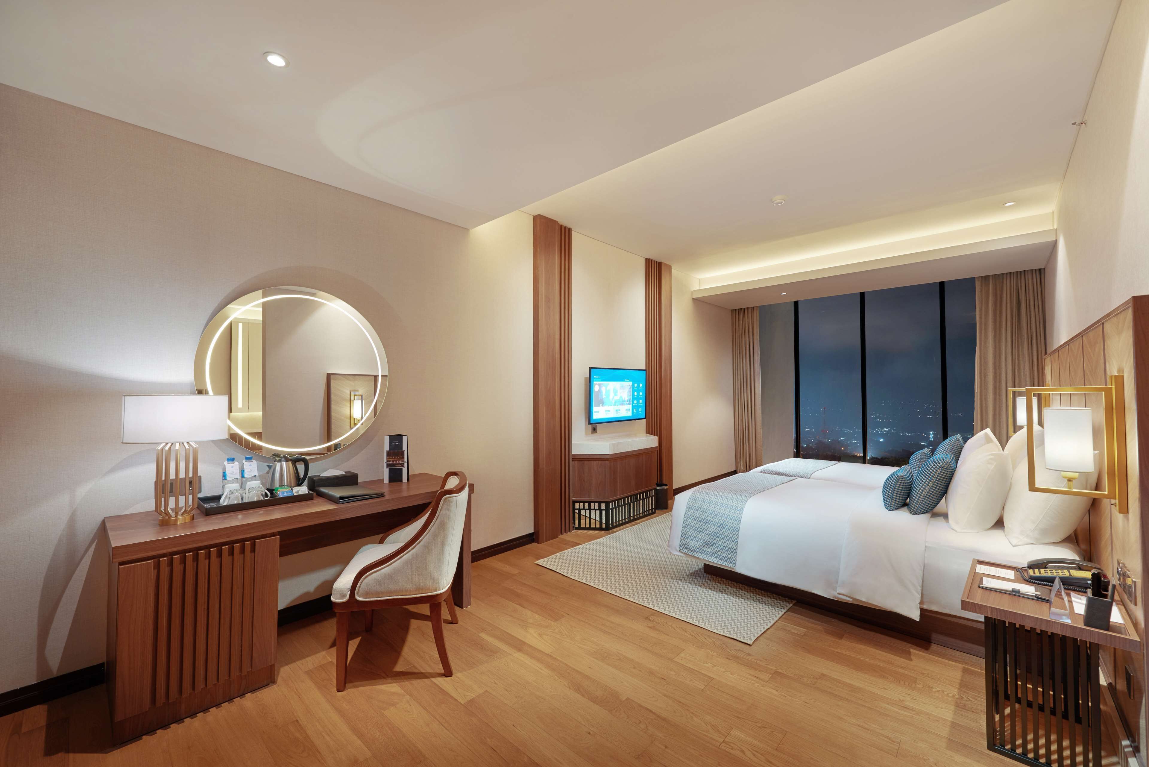 Una habitación de hotel con cama, escritorio, silla, televisión y un ventanal grande.