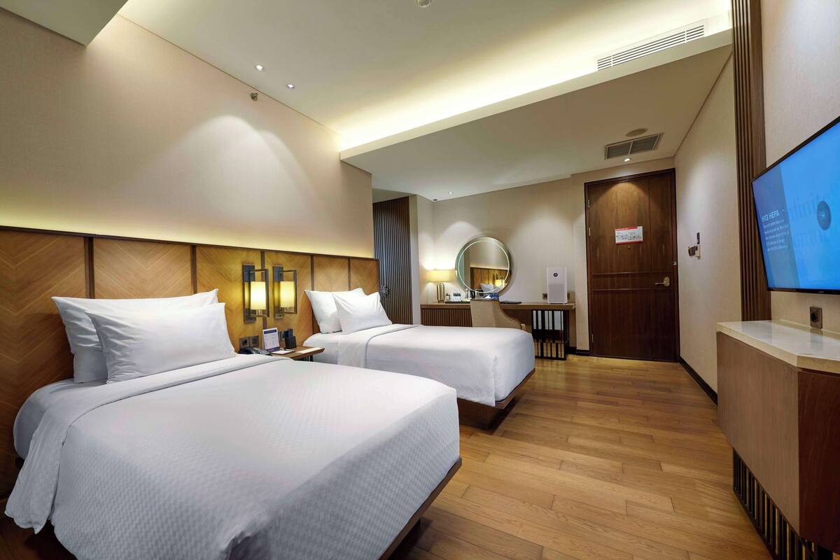 A hotel room with two beds, a desk, a mirror, and a TV.