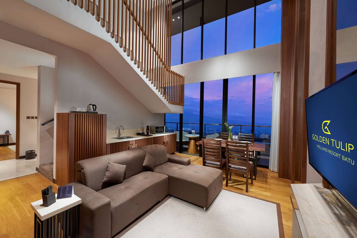 A modern living room with a sectional sofa, a dining area, and a staircase leading to an upper level.