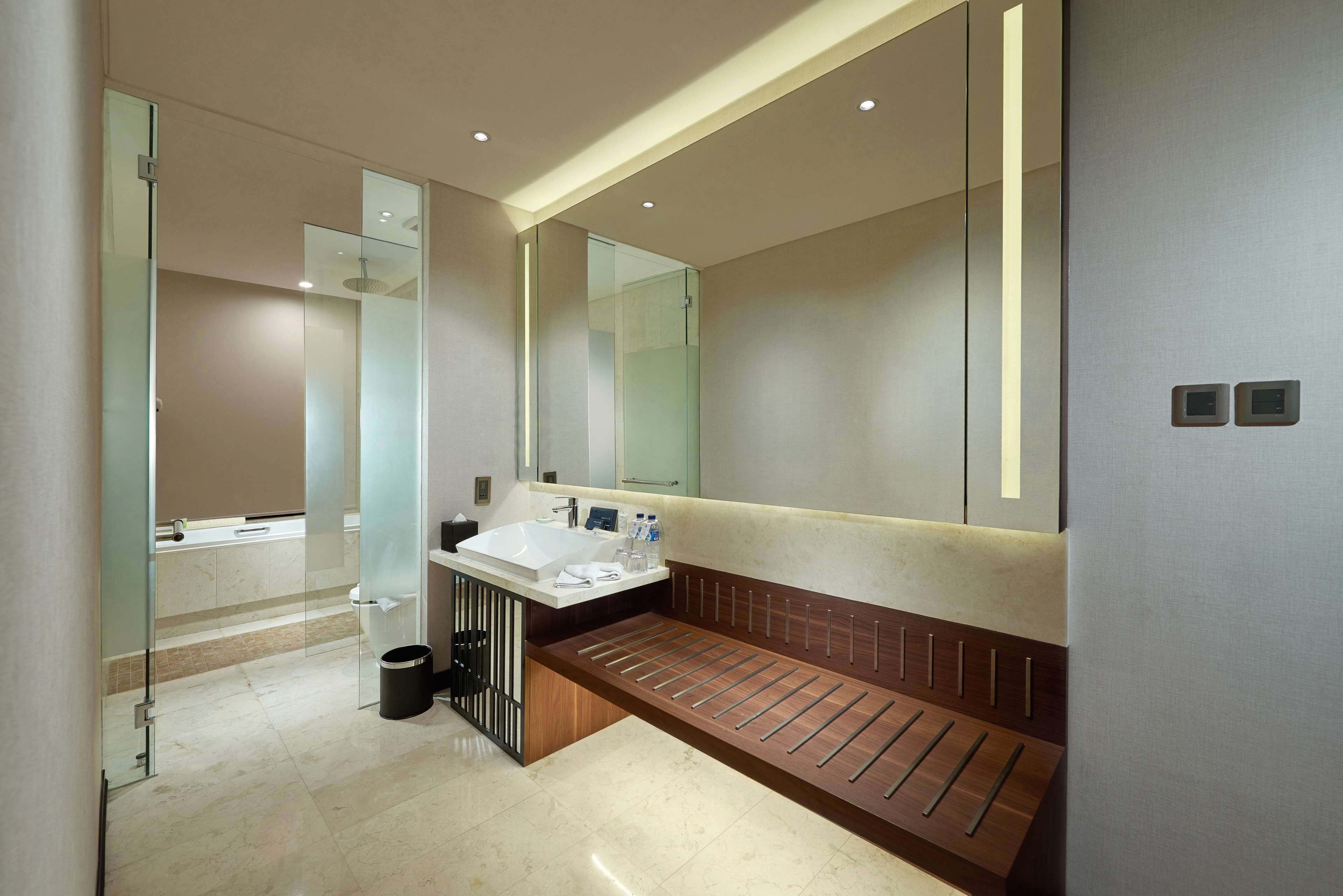 Un baño moderno con cabina de ducha de vidrio, un banco de madera y un espejo grande.