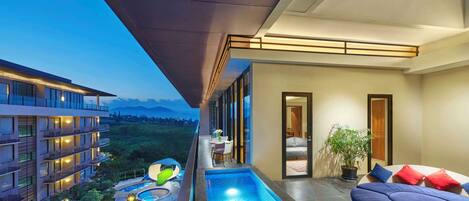 Un balcón de hotel moderno con piscina, mobiliario exterior y vistas del paisaje circundante.
