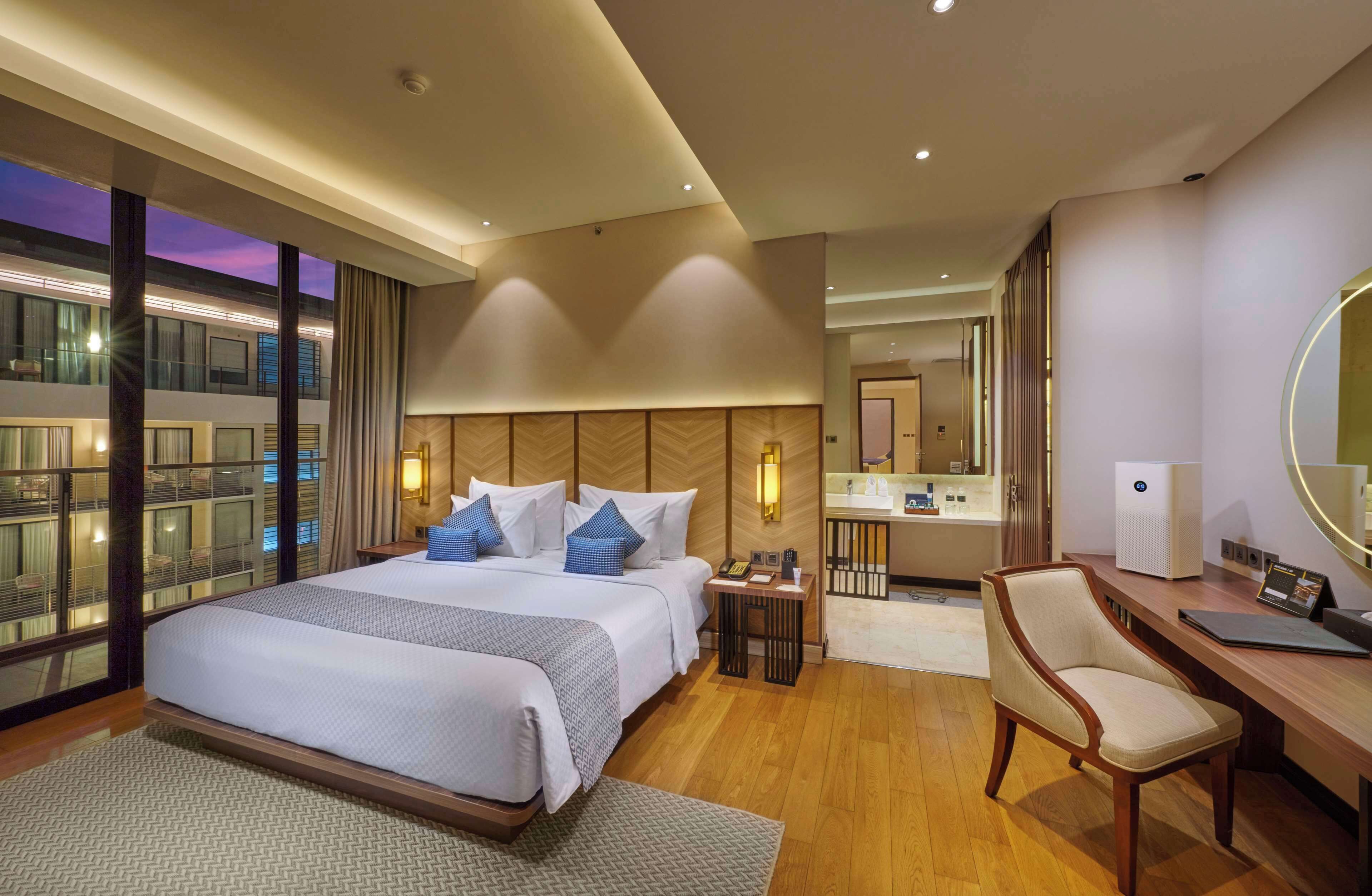 Habitación de hotel con una cama grande, un escritorio, una silla, baño y vistas a la ciudad.