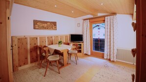 A cozy room with wooden walls and ceiling, a dining table with chairs, a TV, and a window with curtains. - Ferienwohnung Ahnenhöfl (Gaschurn)