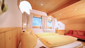A cozy room with a wooden ceiling, a bed with yellow checkered bedding, a red sofa, and a window with curtains. - Ferienwohnung Ahnenhöfl (Gaschurn)