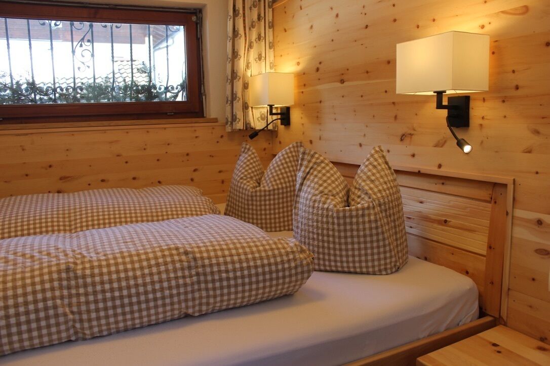 Ein Zimmer einer Holzhütte mit zwei Betten, karierten Bettbezügen, einem Fenster mit Vorhang und zwei Wandleuchten.
