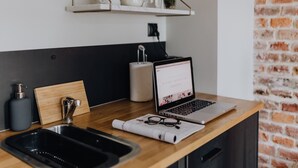 A kitchen counter with a laptop, a sink, and a wooden cutting board. - Well Well Aparthotel (Kraków)