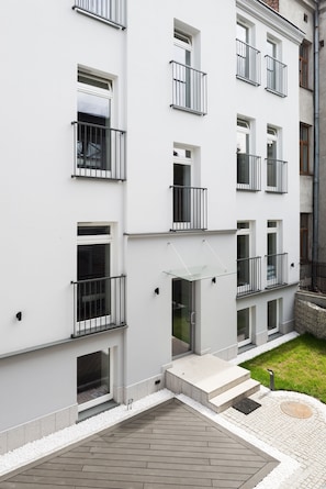 A multi-story building with balconies, a small garden area, and a paved entrance.