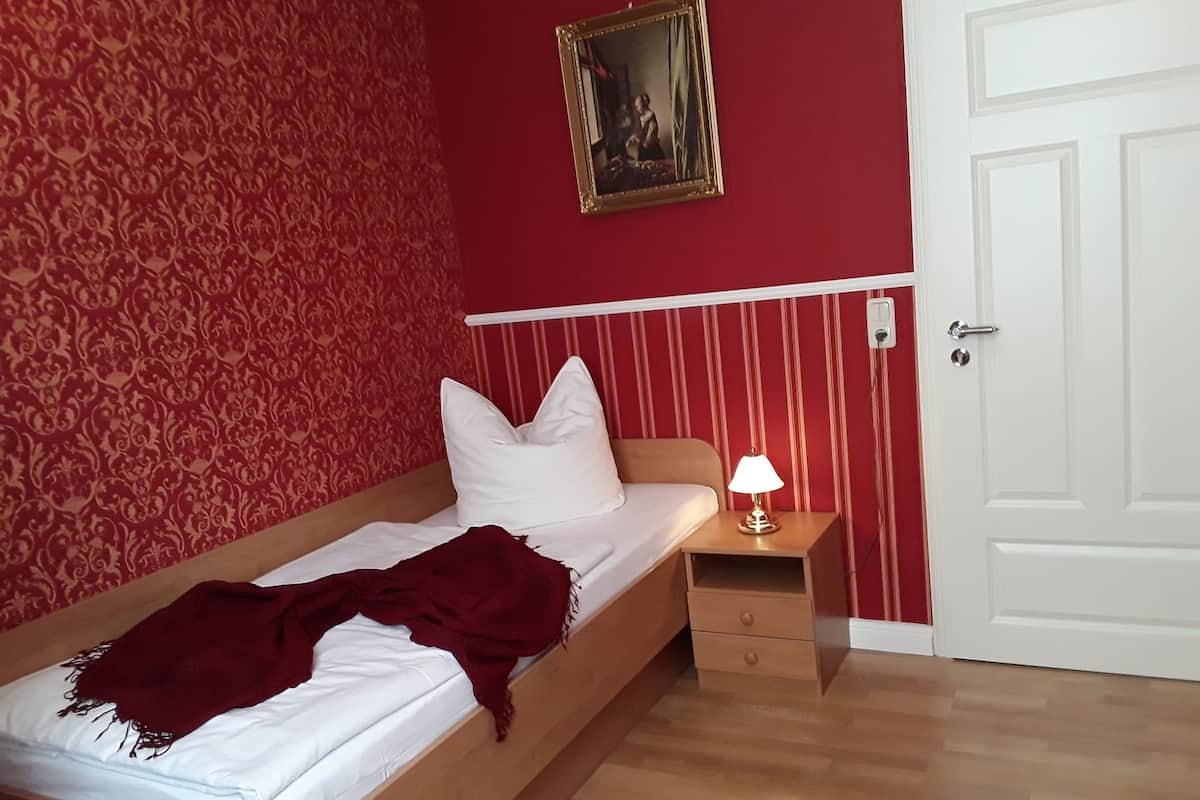 Une pièce avec un lit, une table de chevet avec une lampe, une porte et un mur décoré de motifs.