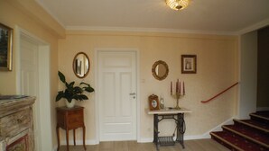 A hallway with a white door, a mirror, a candelabra, and a staircase.