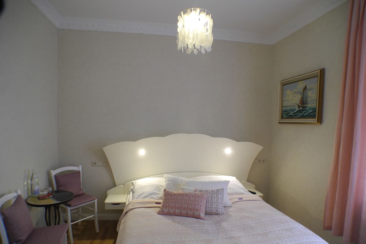 Une chambre à coucher avec un lit, une chaise, une table, un lustre et un tableau accroché au mur.