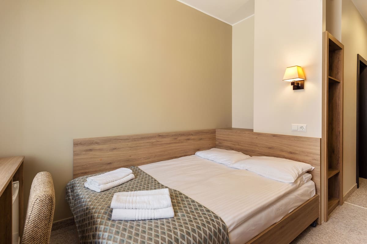 A neatly made bed with a patterned bedspread and two pillows, a bedside table, a lamp, and a wooden headboard.