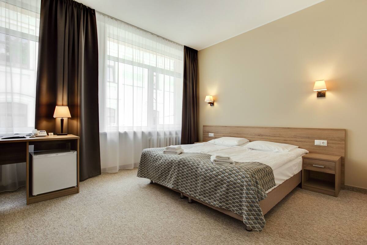 A hotel room with a bed, bedside tables, a desk, and a lamp.